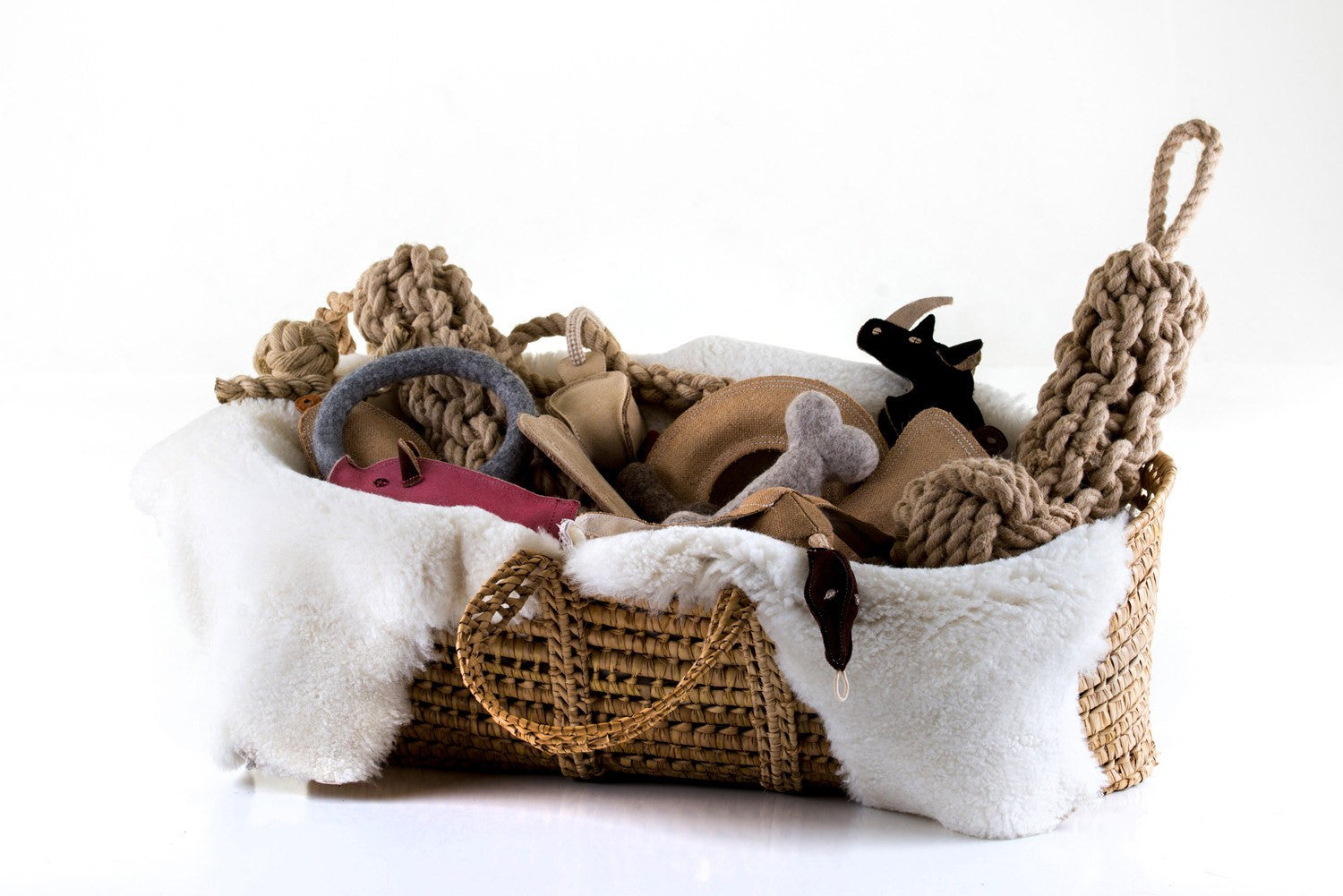 Hand made raffia dog toy basket filled with toys and a sheepskin